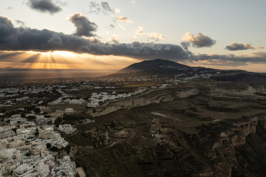Aerial view of sunlight piercing through dark clouds over the whitewashed buildings of Santorini and the rugged landscape Thira Greece. Aerial view of sunlight piercing through dark clouds over the whitewashed buildings of Santorini and the rugged landscape Thira Greece.