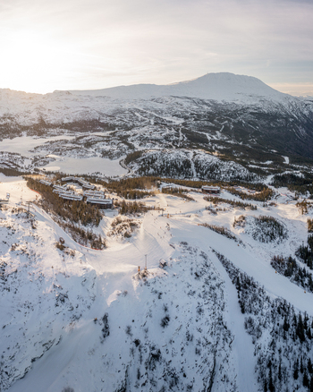 Aerial view of Gaustablikk Fjellresort nestled in the snowy mountains of Telemark with ski slopes and pine trees under the golden hour light in Rjukan Telemark Norway. Aerial view of Gaustablikk Fjellresort nestled in the snowy mountains of Telemark with ski slopes and pine trees under the golden hour light in Rjukan Telemark Norway.