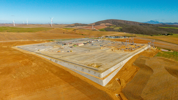 Aerial view of an electrical substation under construction surrounded by dry fields and wind turbines under a clear blue sky in Swellendam Western Cape South Africa. Aerial view of an electrical substation under construction surrounded by dry fields and wind turbines under a clear blue sky in Swellendam Western Cape South Africa.