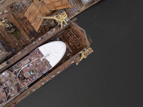 Aerial view of a large ship under construction in a dry dock at the shipyard with industrial cranes and metal structures in Gdansk Poland. Aerial view of a large ship under construction in a dry dock at the shipyard with industrial cranes and metal structures in Gdansk Poland.