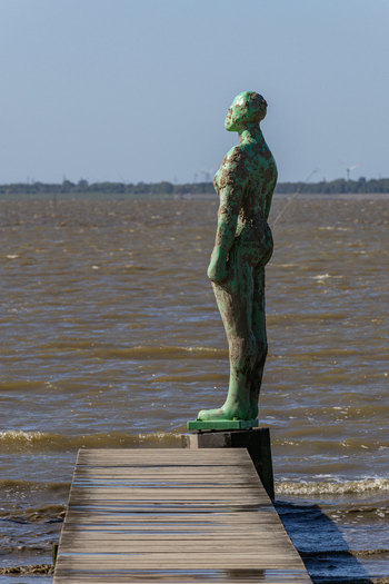 View of a green weathered sculpture standing at the end of a wooden pier overlooking the sea in Dangast Varel Lower Saxony Germany. View of a green weathered sculpture standing at the end of a wooden pier overlooking the sea in Dangast Varel Lower Saxony Germany.