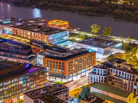 Aerial view of the Copernicus Science Centre and the University of Warsaw Library among modern illuminated buildings along the Vistula riverbank at night in Poland. Aerial view of the Copernicus Science Centre and the University of Warsaw Library among modern illuminated buildings along the Vistula riverbank at night in Poland.