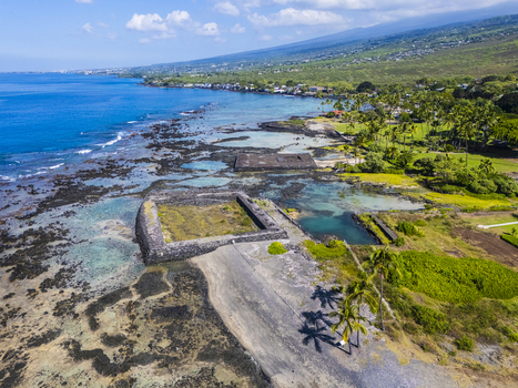 Aerial view of the ancient stone heiau at Kahaluu Beach Park along the rocky lava coastline with palm trees and turquoise water in Kailua Kona Hawaii United States. Aerial view of the ancient stone heiau at Kahaluu Beach Park along the rocky lava coastline with palm trees and turquoise water in Kailua Kona Hawaii United States.