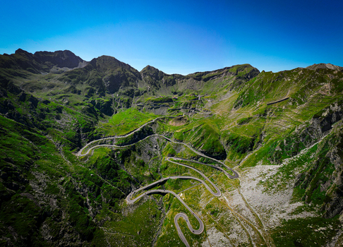Aerial view of the winding Transfagarasan mountain road cutting through the lush green Fagaras Mountains under a clear blue sky in Curtea de Arges Judetul Arges Romania. Aerial view of the winding Transfagarasan mountain road cutting through the lush green Fagaras Mountains under a clear blue sky in Curtea de Arges Judetul Arges Romania.