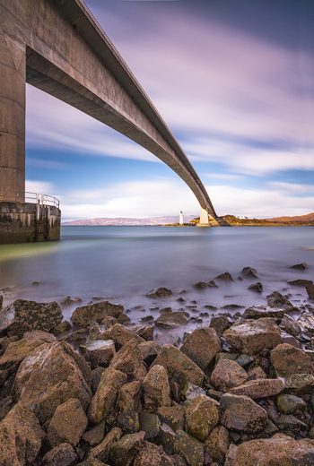 View of the Skye Bridge spanning the water with rocky foreground and soft clouds at sunset in Isle of Skye United Kingdom. View of the Skye Bridge spanning the water with rocky foreground and soft clouds at sunset in Isle of Skye United Kingdom.