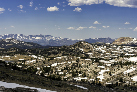 Aerial view of Beartooth Pass featuring rugged mountain terrain with patches of snow evergreen trees and rocky slopes in Park County Wyoming United States. Aerial view of Beartooth Pass featuring rugged mountain terrain with patches of snow evergreen trees and rocky slopes in Park County Wyoming United States.