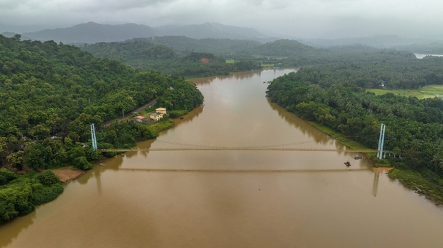 Aerial view of the suspension bridge spanning the Sharavathi River surrounded by lush green hills and dense vegetation under an overcast sky in Honnavar Karnataka India.
