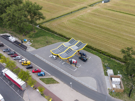 Aerial view of Fastned charging station with solar panel roof and electric vehicles parked in charging bays located near a road and green fields in Breukelen Utrecht Netherlands. Aerial view of Fastned charging station with solar panel roof and electric vehicles parked in charging bays located near a road and green fields in Breukelen Utrecht Netherlands.