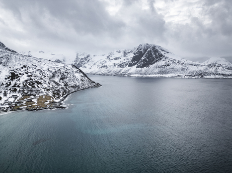 Aerial view of Grotfjord with snow covered mountains and dark blue water under a cloudy sky in Tromvik Troms Norway. Aerial view of Grotfjord with snow covered mountains and dark blue water under a cloudy sky in Tromvik Troms Norway.