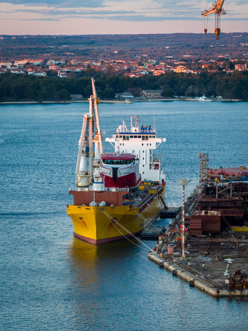 Aerial view of the Uljanik Shipyard with a large yellow cargo ship docked at the pier and industrial cranes in Pula Croatia. Aerial view of the Uljanik Shipyard with a large yellow cargo ship docked at the pier and industrial cranes in Pula Croatia.