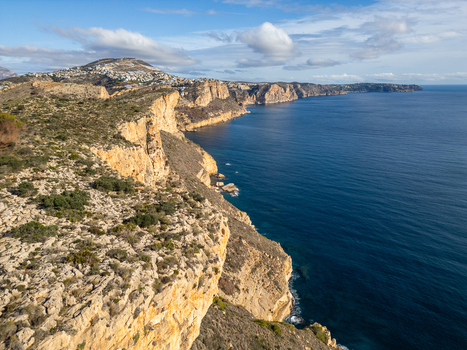 Aerial view of Cala Llebeig with rugged limestone cliffs dropping into the Mediterranean Sea under a clear sky. El Poble Nou de Benitatxell Valencian Community Spain.