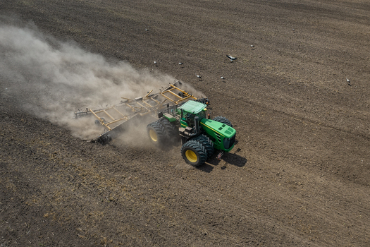 Aerial view of a green and yellow tractor churning up dark earth creating a cloud of dust as it tills the soil Chyhyryns kyi district Cherkasy Oblast Ukraine. Aerial view of a green and yellow tractor churning up dark earth creating a cloud of dust as it tills the soil Chyhyryns kyi district Cherkasy Oblast Ukraine.
