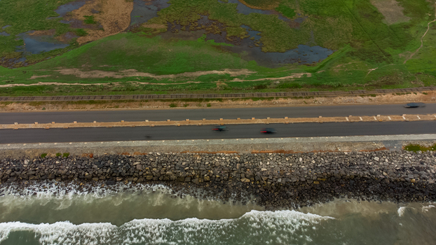 Aerial view of Accra Tema Beach Road featuring a coastal highway with rocky shoreline crashing waves adjacent railway tracks and green landscape in Accra Greater Accra Region Ghana.