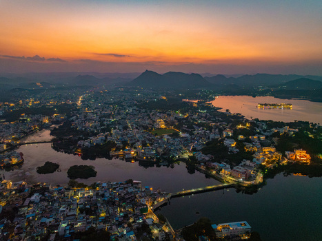 Aerial view of Lake Pichola at sunset with glowing city lights reflecting on the water Udaipur Rajasthan India.