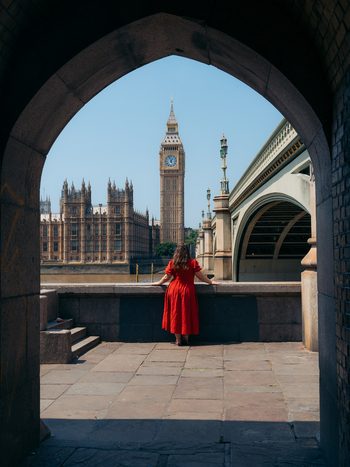 View of a vibrant red clad figure framed by an archway gazing across the Thames at Big Ben and Parliament London England United Kingdom. View of a vibrant red clad figure framed by an archway gazing across the Thames at Big Ben and Parliament London England United Kingdom.