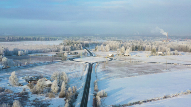 Aerial view of a roundabout surrounded by snow covered fields and frost covered trees under a clear sky in Latvia. Aerial view of a roundabout surrounded by snow covered fields and frost covered trees under a clear sky in Latvia.