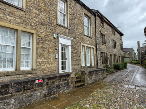 View of traditional stone cottages along a narrow cobblestone street under an overcast sky in Hawes England United Kingdom. View of traditional stone cottages along a narrow cobblestone street under an overcast sky in Hawes England United Kingdom.