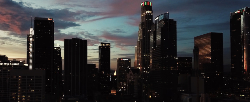 Aerial view of the Los Angeles skyline featuring illuminated skyscrapers and modern office buildings under a colorful sunset sky in Los Angeles California United States.