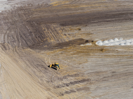 Aerial view of Tagebau Welzow Sud brown coal open pit mine with a yellow bulldozer working on the vast excavated landscape showing soil tracks in Spremberg Brandenburg Germany. Aerial view of Tagebau Welzow Sud brown coal open pit mine with a yellow bulldozer working on the vast excavated landscape showing soil tracks in Spremberg Brandenburg Germany.