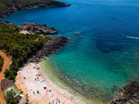 Aerial view of Aquarium Beach with turquoise waters rocky cliffs and lush green hills in Jala Vlore County Albania.