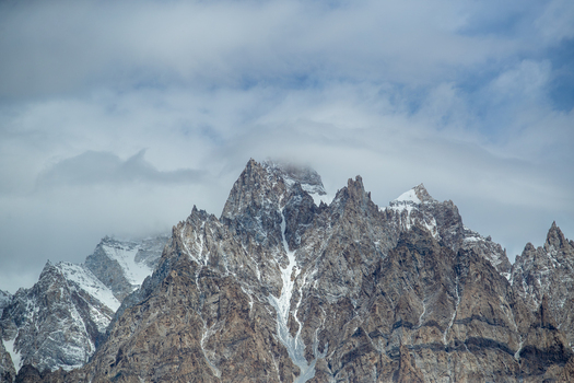 View of the jagged snow dusted peaks of the Passu Cones partially obscured by clouds in Passu Gilgit Pakistan. View of the jagged snow dusted peaks of the Passu Cones partially obscured by clouds in Passu Gilgit Pakistan.
