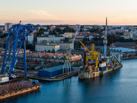 Aerial view of Uljanik Shipyard with large blue and yellow cranes industrial machinery and ships docked in the harbor at sunset in Pula Croatia. Aerial view of Uljanik Shipyard with large blue and yellow cranes industrial machinery and ships docked in the harbor at sunset in Pula Croatia.