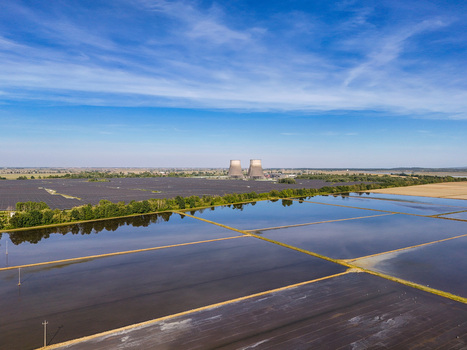 Aerial view of Tenuta Colombara flooded rice fields reflecting the blue sky with cooling towers and a solar farm in the distance Livorno Ferraris Piemonte Italy.