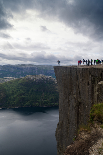 View of Pulpit Rock with tourists standing on the edge overlooking the Lysefjord under a cloudy sky in Strand Rogaland Norway. View of Pulpit Rock with tourists standing on the edge overlooking the Lysefjord under a cloudy sky in Strand Rogaland Norway.