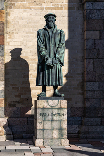 View of the bronze statue of Hans Tausen holding a book in front of a brick wall at Ribe Cathedral Ribe Denmark. View of the bronze statue of Hans Tausen holding a book in front of a brick wall at Ribe Cathedral Ribe Denmark.