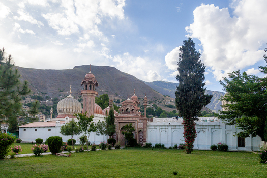 View of the historic Shahi Mosque with its distinctive domes and minarets set against a backdrop of mountains and a lush green lawn in Chitral Khyber Pakhtunkhwa Pakistan.