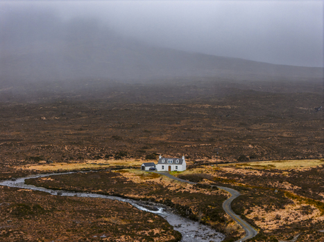 Aerial view of a white cottage nestled in the rugged moorland landscape with a winding road and stream under misty hills Isle of Skye Scotland United Kingdom. Aerial view of a white cottage nestled in the rugged moorland landscape with a winding road and stream under misty hills Isle of Skye Scotland United Kingdom.