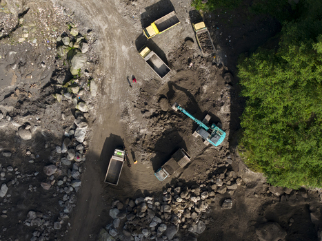 Aerial view of Tambang Pasir Merapi Kali Gendol Sand Mine with an excavator loading trucks and workers on the ground in Kecamatan Cangkringan Daerah Istimewa Yogya Indonesia. Aerial view of Tambang Pasir Merapi Kali Gendol Sand Mine with an excavator loading trucks and workers on the ground in Kecamatan Cangkringan Daerah Istimewa Yogya Indonesia.