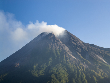 Aerial view of Mount Merapi with smoke rising from the crater and lush green slopes under a clear blue sky Kecamatan Pakem Daerah Istimewa Yogya Indonesia. Aerial view of Mount Merapi with smoke rising from the crater and lush green slopes under a clear blue sky Kecamatan Pakem Daerah Istimewa Yogya Indonesia.