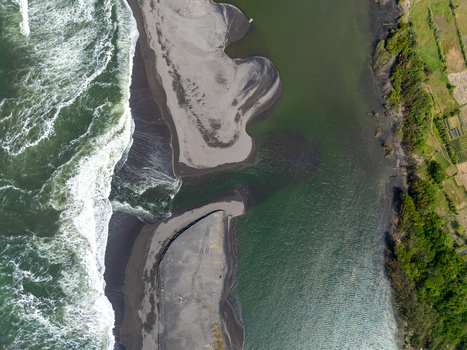 Aerial view of Depok Beach where the river meets the ocean with dark sand banks and lush green vegetation in Special Region of Yogyakarta Indonesia. Aerial view of Depok Beach where the river meets the ocean with dark sand banks and lush green vegetation in Special Region of Yogyakarta Indonesia.