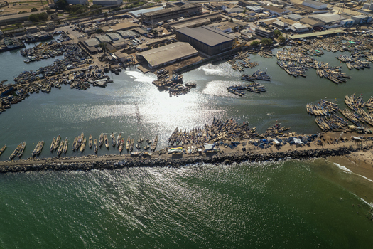 Aerial view of countless fishing boats clustered tightly in the harbor creating a mosaic of hulls and masts under the sun s shimmering reflection Tema Ghana. Aerial view of countless fishing boats clustered tightly in the harbor creating a mosaic of hulls and masts under the sun s shimmering reflection Tema Ghana.