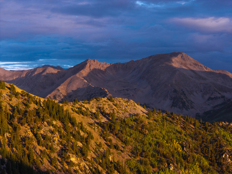 Aerial view of Missouri Mountain and rugged Sawatch Range peaks in golden morning light with evergreen forests and dramatic clouds in Buena Vista Colorado United States.