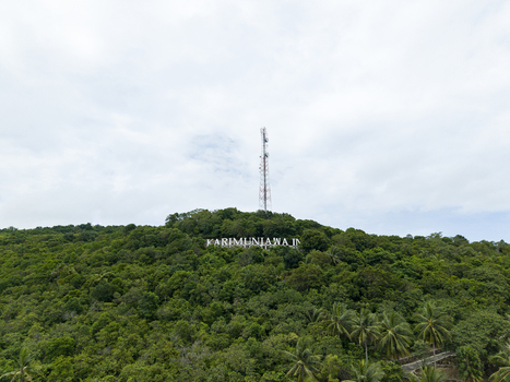 Aerial view of lush green hill crowned with the sign KARIMUNJAWA I and a telecommunications tower piercing the skyline Karimunjawa Central Java Indonesia. Aerial view of lush green hill crowned with the sign KARIMUNJAWA I and a telecommunications tower piercing the skyline Karimunjawa Central Java Indonesia.