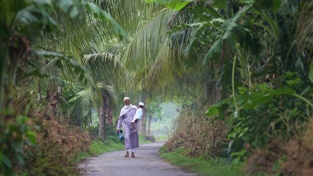 View of a man carrying a child on a path with palm trees Bangladesh. View of a man carrying a child on a path with palm trees Bangladesh.