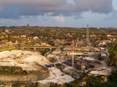 Aerial view of a resort development construction site with a red crane excavation and limestone cliffs near residential buildings in Kecamatan Kuta Selatan Bali Indonesia. Aerial view of a resort development construction site with a red crane excavation and limestone cliffs near residential buildings in Kecamatan Kuta Selatan Bali Indonesia.