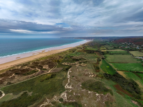 Aerial view of Dunes de Biville featuring expansive sandy dunes lush green fields and the coastline meeting the Atlantic Ocean under a cloudy sky in La Hague Normandie France.