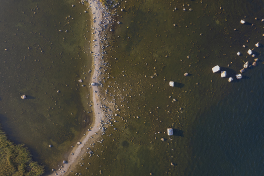 Aerial view of Kuradi saar featuring a rocky spit extending into the shallow coastal waters with scattered boulders and reeds in Kasmu Laane Viru County Estonia.