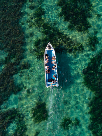 Aerial view of a small boat carrying passengers across the clear turquoise waters of the ocean with visible seaweed patches in Kecamatan Denpasar Selatan Bali Indonesia.