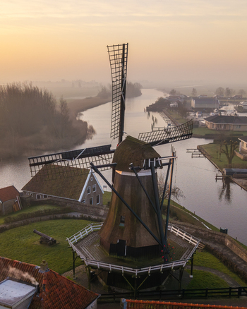 Aerial view of a traditional windmill standing by a misty canal during a golden sunrise in Sloten Friesland Netherlands. Aerial view of a traditional windmill standing by a misty canal during a golden sunrise in Sloten Friesland Netherlands.
