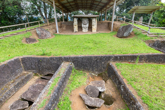 View of ancient stone statues at San Agustin Archaeological Park set within a grassy burial site under a protective roof structure in San Agustin Huila Colombia.
