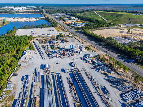 Aerial view of an industrial concrete bridge manufacturing facility with rows of steel I beams heavy machinery and storage yards in Wilmington North Carolina United States. Aerial view of an industrial concrete bridge manufacturing facility with rows of steel I beams heavy machinery and storage yards in Wilmington North Carolina United States.