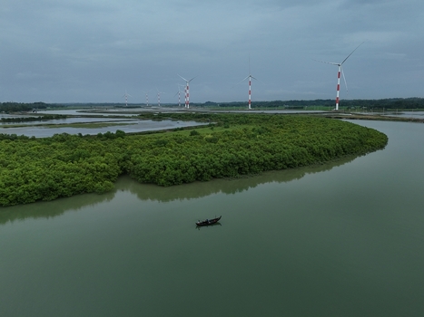 Aerial view of the Khurushkul wind farm with turbines rising above mangrove forests and a small fishing boat on the river in Cox s Bazar Chittagong Division Bangladesh. Aerial view of the Khurushkul wind farm with turbines rising above mangrove forests and a small fishing boat on the river in Cox s Bazar Chittagong Division Bangladesh.