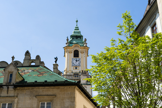 View of the historic Old Town Hall clock tower with its green copper roof and a vibrant green tree under a clear blue sky in Bratislava Bratislava Region Slovakia. View of the historic Old Town Hall clock tower with its green copper roof and a vibrant green tree under a clear blue sky in Bratislava Bratislava Region Slovakia.