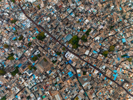 Aerial view of the dense urban fabric of Udaipur featuring traditional rooftops narrow streets and scattered green trees in Udaipur Rajasthan India.