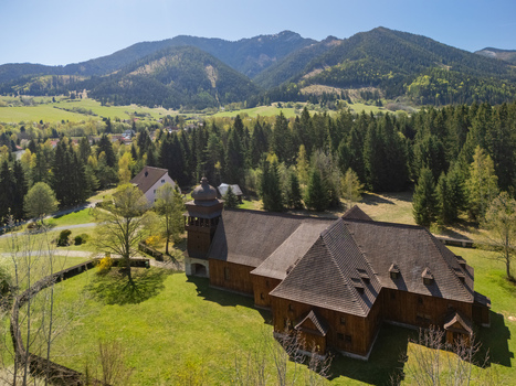 Aerial view of the Wooden Articular Church of Svaty Kriz surrounded by green meadows and dense forests with mountains in the background in Svaty Kriz Zilinsky kraj Slovakia.
