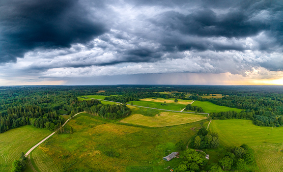 Aerial view of a rural landscape in Latvia featuring lush green fields patches of forest and a winding road under a dramatic dark storm sky with rain clouds in the distance Latvia. Aerial view of a rural landscape in Latvia featuring lush green fields patches of forest and a winding road under a dramatic dark storm sky with rain clouds in the distance Latvia.
